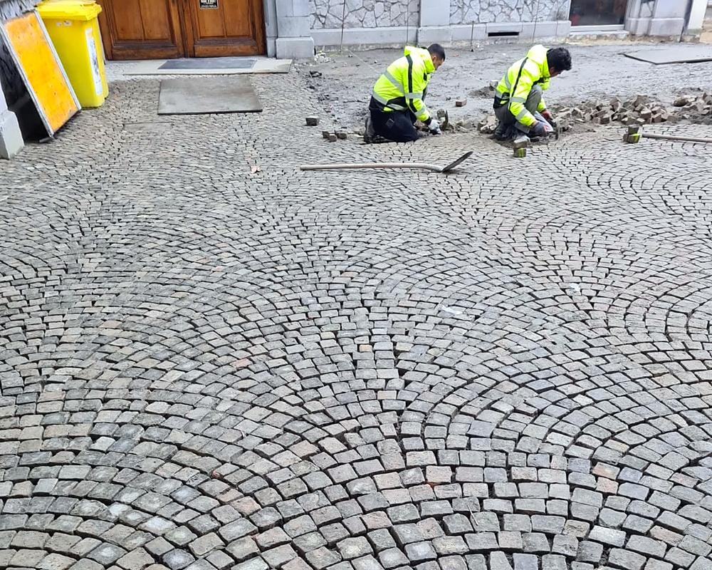 Deux paveurs posant des pavés gris en queue de paon dans une cour