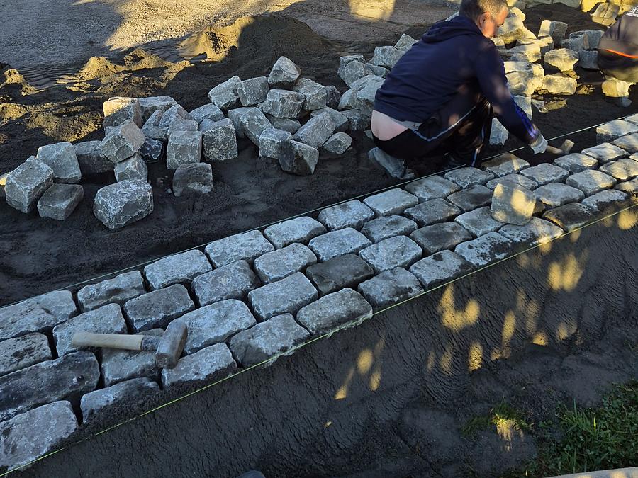 Paveur posant une bordure de pavés le long d'une maison en pierre
