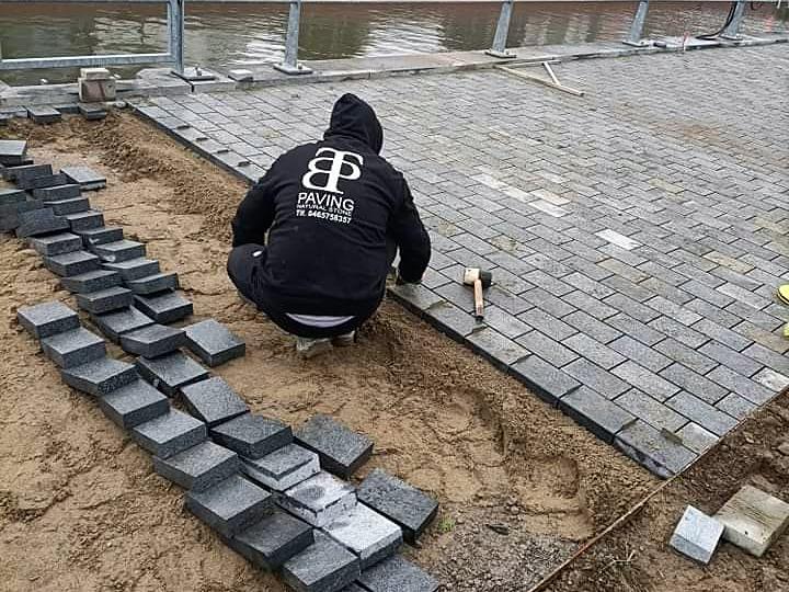 Paveur TBP Paving posant des pavés foncés le long d'un quai